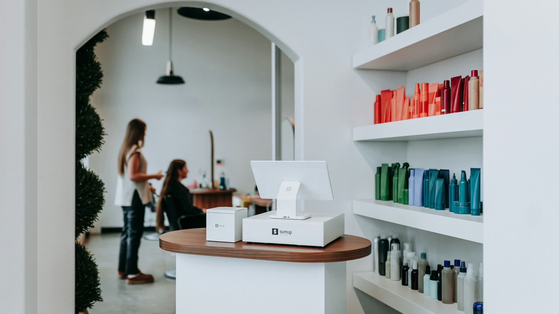 A salon reception with styling products, a stylist working with a client behind
